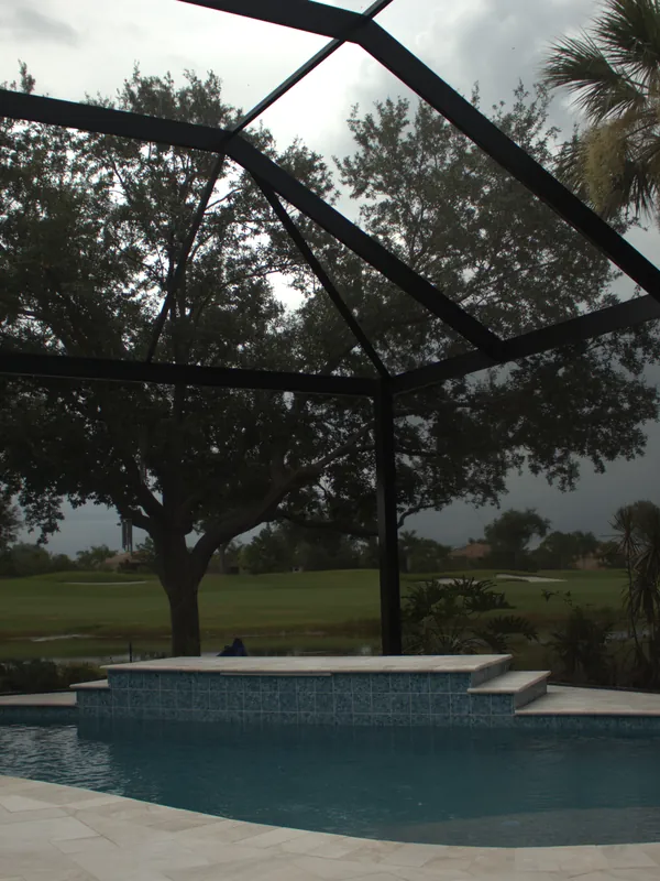 View from inside a clear-span cage toward the pool, spa, and oaks beyond