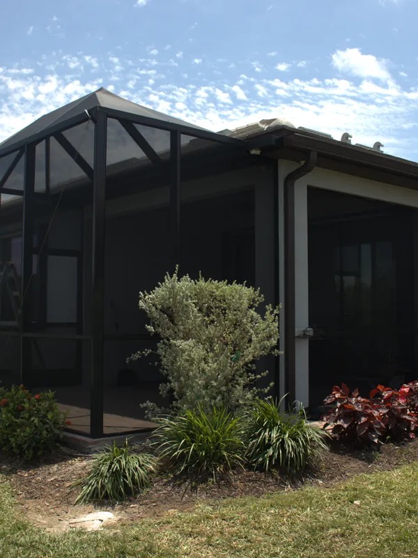 Gable-roof screen enclosure over a lanai, garden beds along the walk