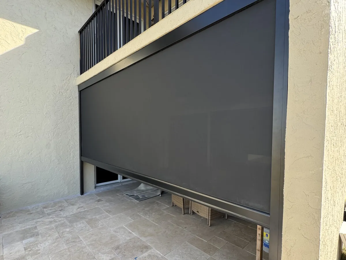 Motorized screen lowered beneath a second-story balcony, enclosing the patio below