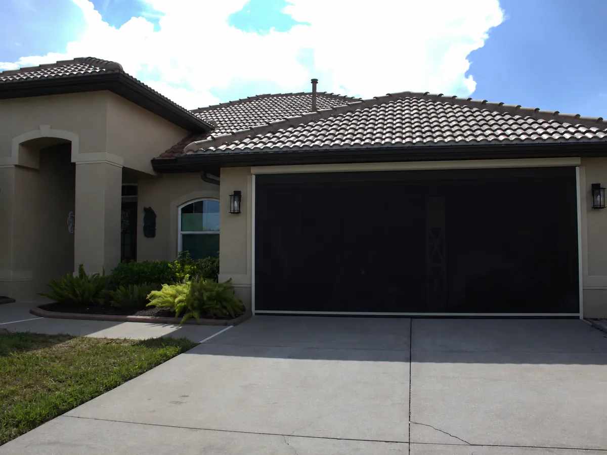 Motorized screen closed across a two-car garage entry, exterior lighting and landscaping framing the door