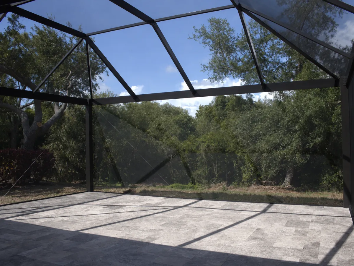 Paver deck laid inside a screened cage, trees beyond