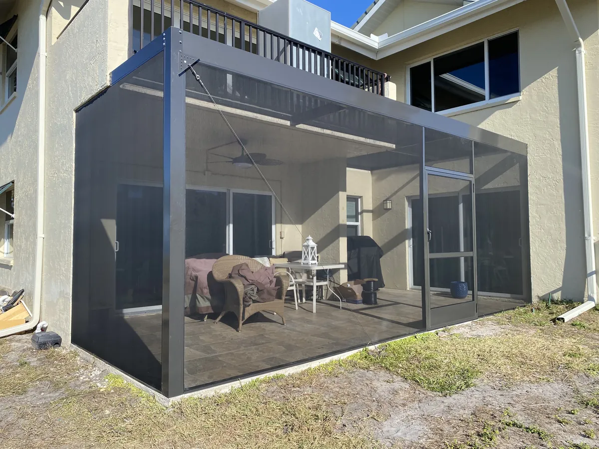Aluminum-framed screen room built beneath a second-story balcony, furnished patio visible inside